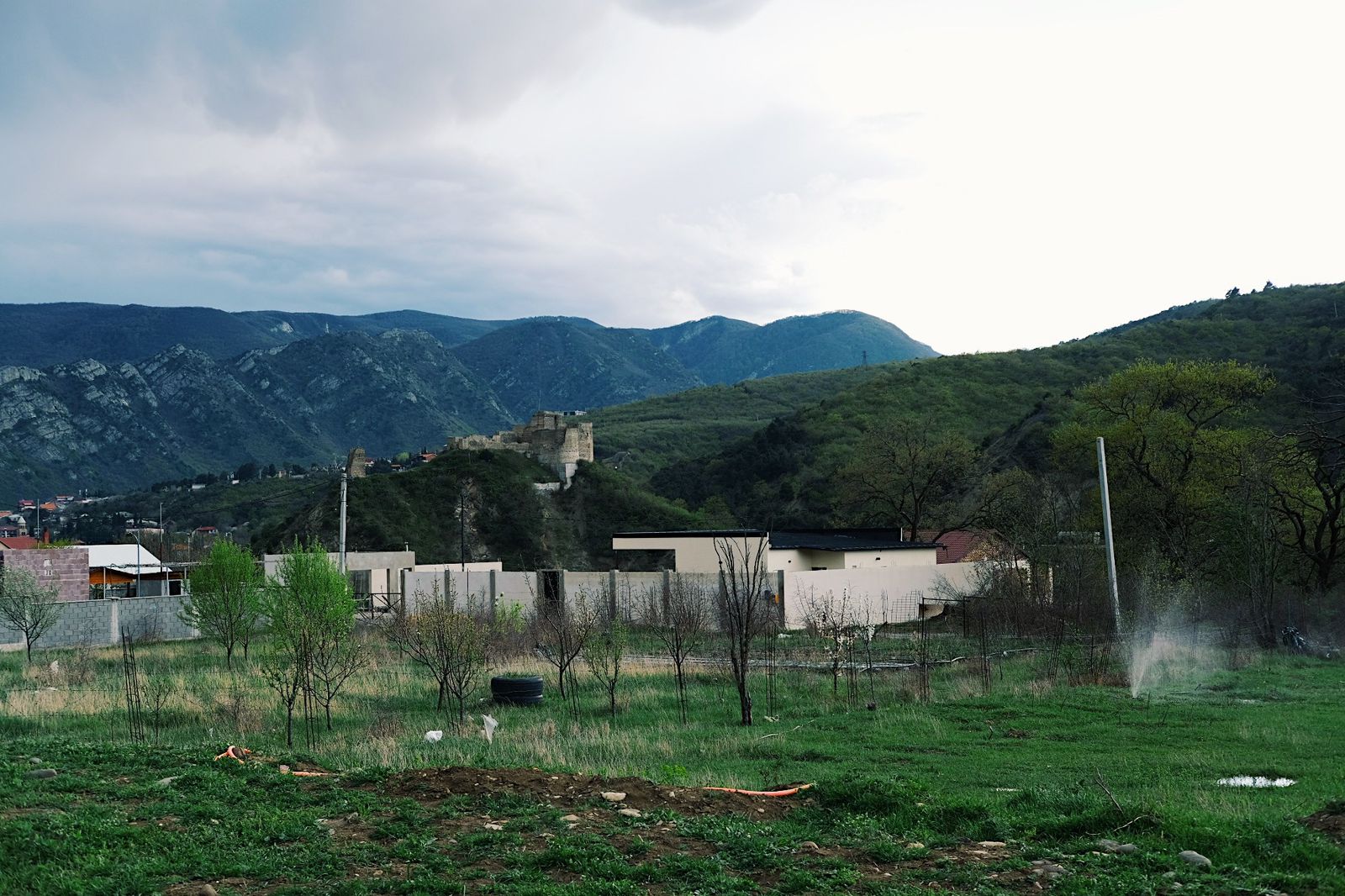 Green camping field facing forested mountains and a hilltop fortress